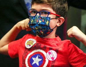 Young child in face mask and super hero pose at Toronto vaccine clinic