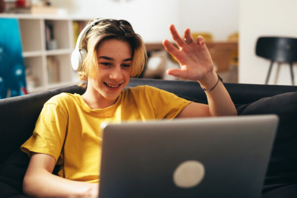 teenage boy with sitting on a sofa and using laptop computer at home for video chatting